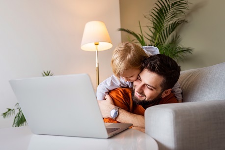 Ein Vater liegt mit seinem Kind auf einem Sofa am Laptop und freut sich &uuml;ber die Er&ouml;ffnung eines Junior Depots f&uuml;r Kinder.